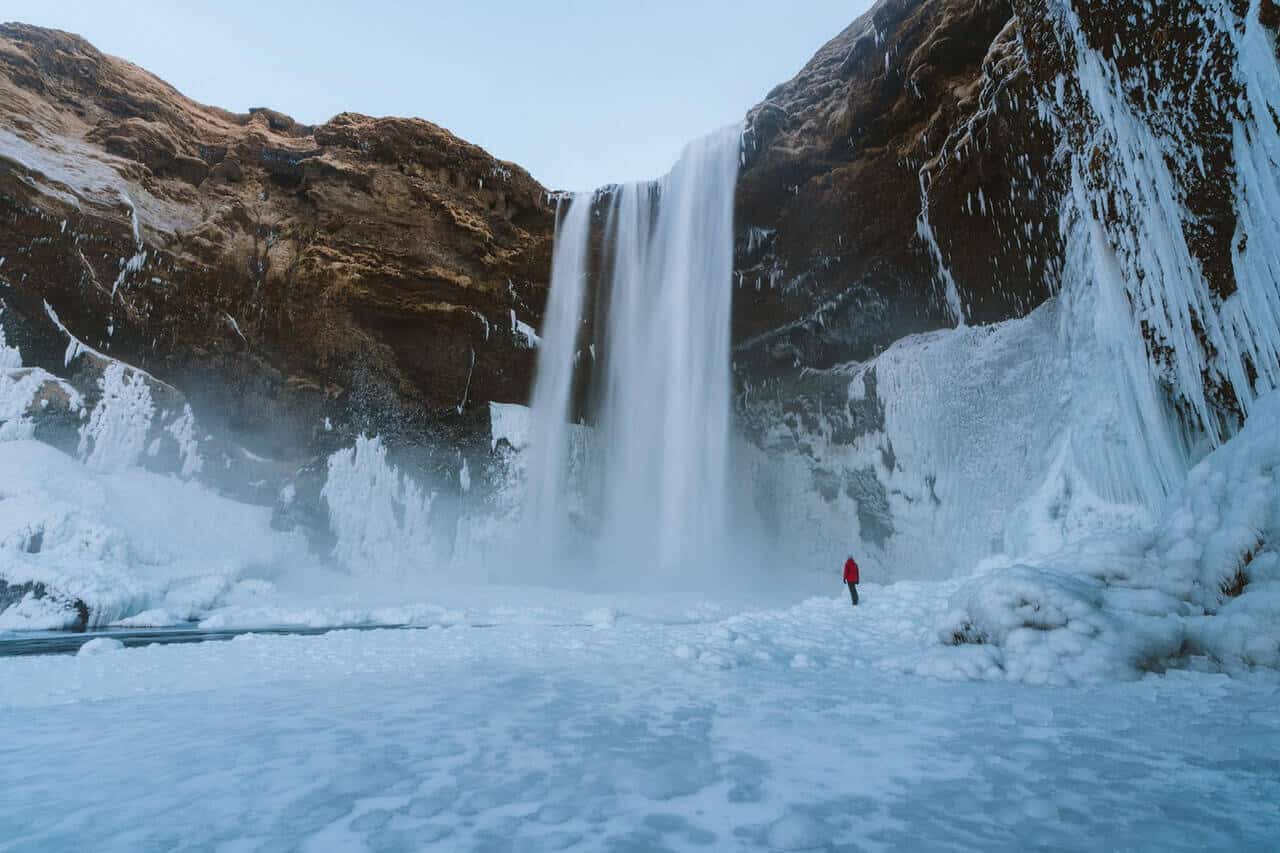 Waterval in IJsland met een persoon die er van dichtbij naar kijkt.