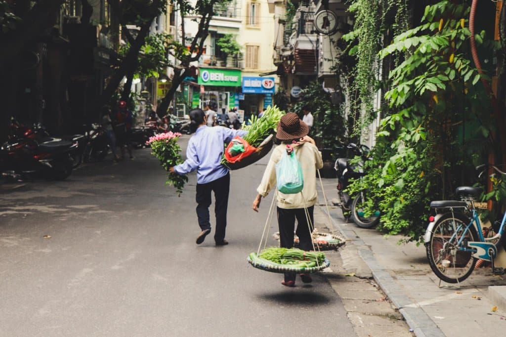 Straat in Vietnam waar een man en een vrouw lopen met hun handelswaar voor op de markt.