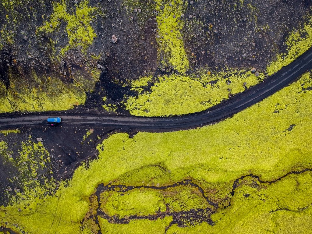 Een weg dwars door de natuur van IJsland met een blauwe auto die erop rijdt.